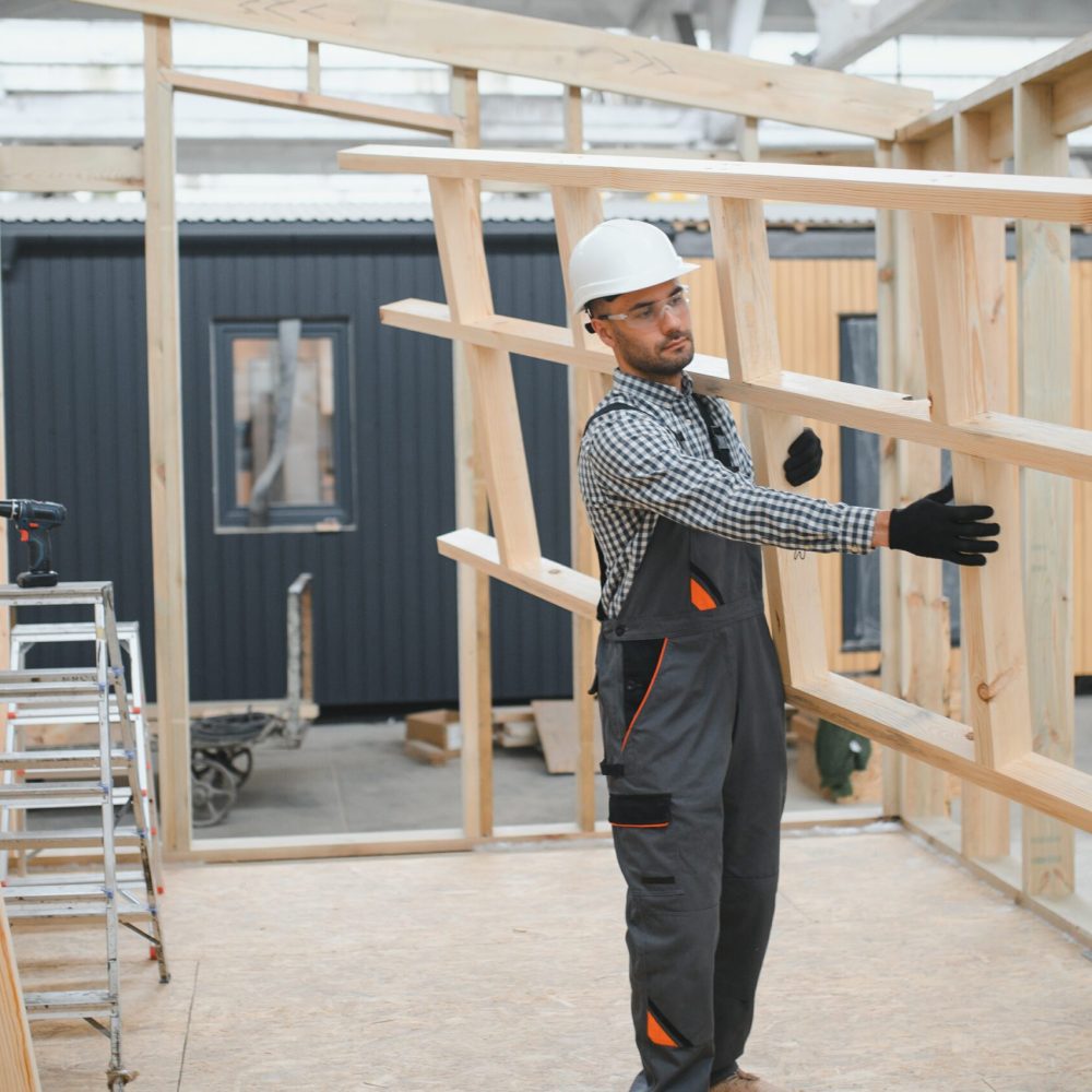 A worker or engineer in a uniform works on a construction site for the manufacture of wooden modular houses.