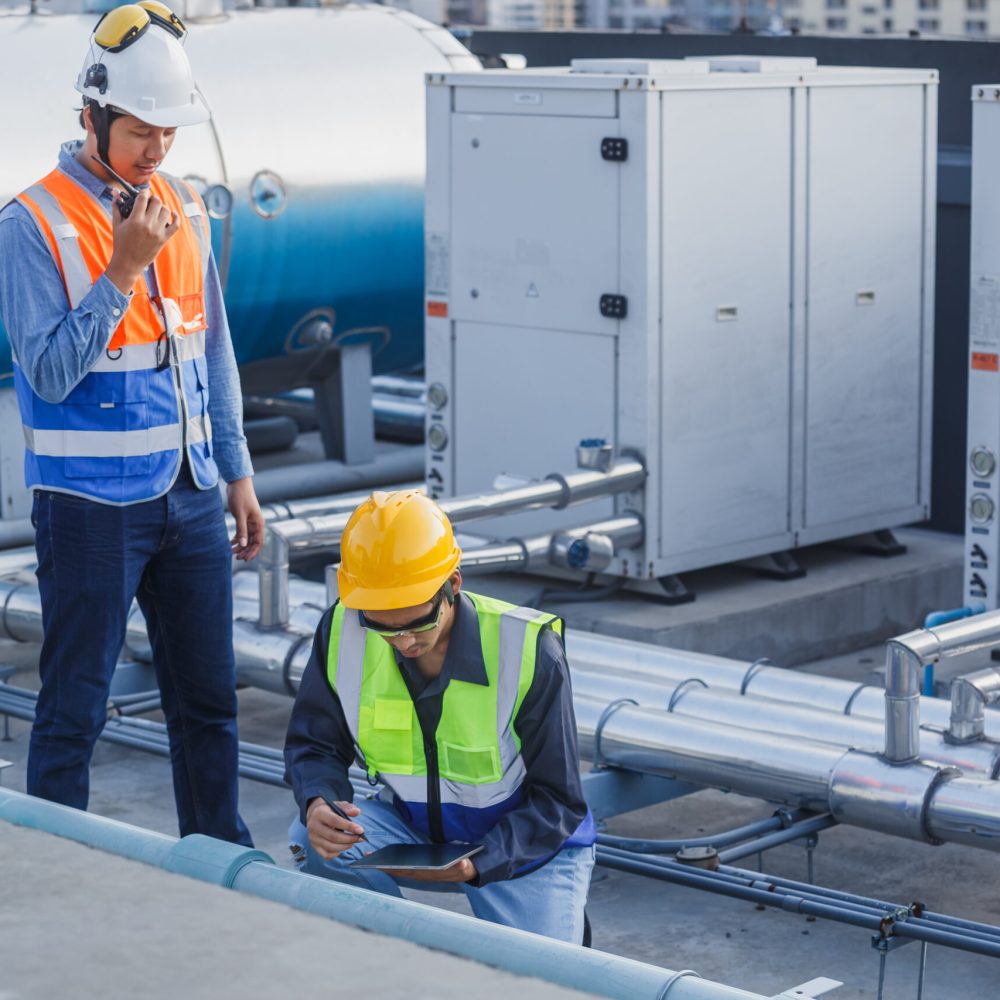 Asian man engineer holding tablet working at rooftop building construction. Male technician worker working checking hvac of office building. Engineering installing large air conditioning system.