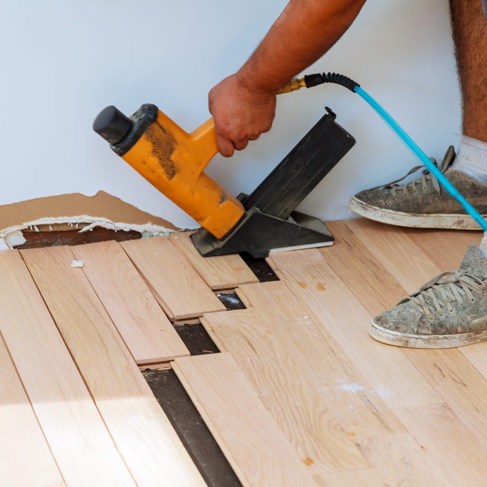 Carpenter worker installing wood parquet board during flooring work with hammer