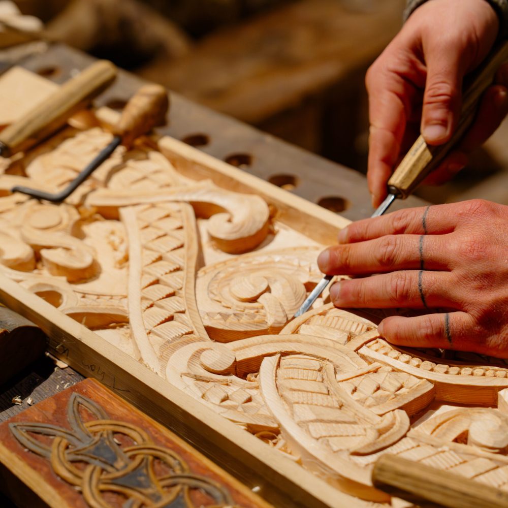 This image features a skilled artisan carpenter meticulously carving ornate and intricate patterns on a wooden surface, highlighting the artistry and precision in woodworking craftsmanship.